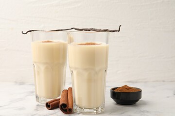 Delicious protein shake in glasses, cinnamon and vanilla pods on white marble table, closeup