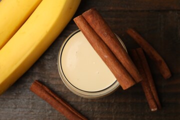 Delicious protein shake in glass, cinnamon and bananas on wooden table, flat lay