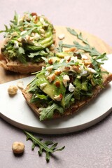 Tasty bruschettas with avocado, arugula, nuts and feta cheese on grey table, closeup