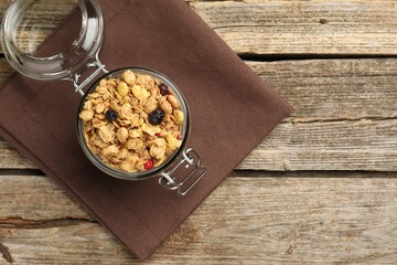 Tasty granola with dried fruits in glass jar on wooden table, top view. Space for text