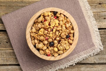 Tasty granola with dried fruits in bowl on wooden table, top view