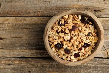 Tasty granola with dried fruits in bowl on wooden table, top view. Space for text