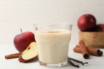 Delicious protein shake in glass, cinnamon, apples and vanilla pods on white table, closeup