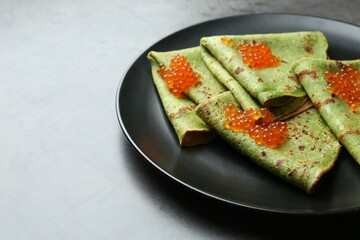 Tasty spinach crepes with red caviar on grey table, closeup. Space for text