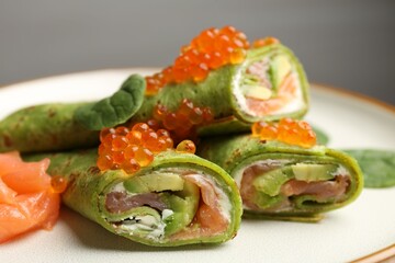 Tasty spinach crepes with salmon, avocado, cream cheese and red caviar on plate, closeup