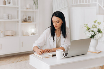 Female Working Diligently, Woman Takes Notes At Her Simple And Bright Workspace Desk, Female Individual Carefully Preparing Her Daily Agenda In Clean Home Office Setting With Technology And Plants