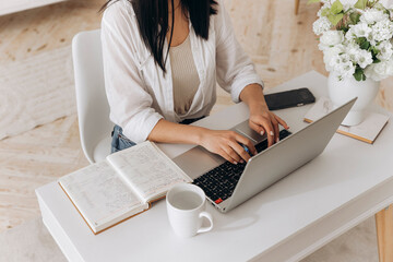 Young brunette freelancer woman sitting at desk using laptop writing notes while studying online, watching webinar, looking at pc screen learning web classes or remote working from home. Side view