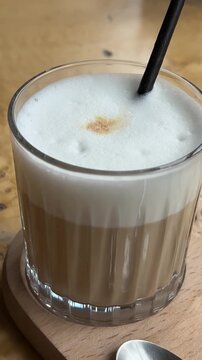 Dolly shot of a clear cup of cappuccino topped with whip cream, cinnamon powder and caramel sauce.