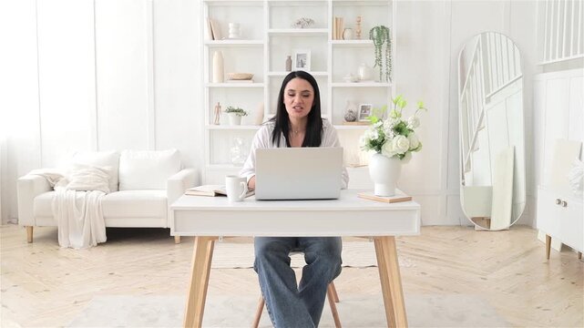 focused caucasian woman at desk, typing on laptop in airy living room, organized planner beside cup, minimalist bright decor, professional remote consultation vibe, calm productivity