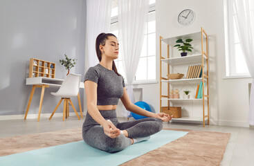Young yogi sporty attractive woman practicing yoga at home doing Ardha Padmasana exercise,...