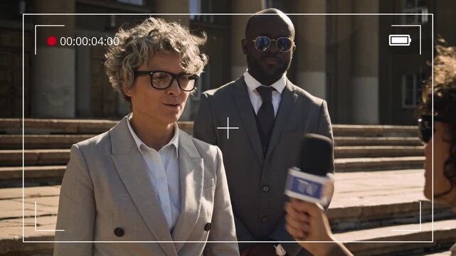Medium shot with video camera frame footage effect of Caucasian female lawyer giving interview to TV journalist near court hall, commenting on trial, protected by bodyguard