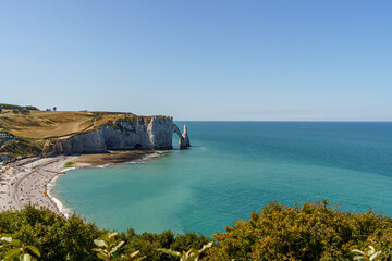 Sarkozy Beach and Rocky Coast, made of stone, extending into the blue water of the ocean in the city of Etretat France The sky is blue The stone arch resembles an elephant's nose