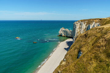 A cliff in the ocean with a rock resembling an elephant in the Etretat, Normandy, France The beach is visible below. And the calm blue water The water is blue, the sky is calm and transparent