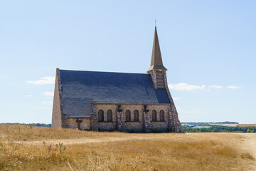 A church in Etretat in France with a steeple is in a field. The church is old and has a weathered appearance. The sky is clear and the sun is shining brightly. Concept of peace and tranquility