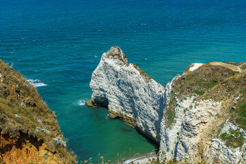 A cliff in the ocean with a rock resembling an elephant in the Etretat, Normandy, France The beach is visible below. And the calm blue water The water is blue, the sky is calm and transparent