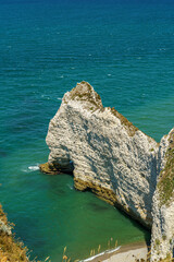 A cliff in the ocean with a rock resembling an elephant in the Etretat, Normandy, France The beach is visible below. And the calm blue water The water is blue, the sky is calm and transparent
