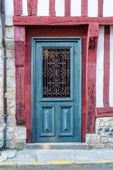 A blue door with a red trim sits in front of a red brick building in Honfleur France Normandy. The door is open and the window is covered with a lattice. The door is a focal point of the image.
