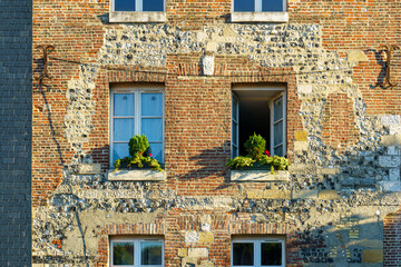 A brick building with two windows and a balcony in Honfleur France Normandy. The windows are open and the balcony has potted plants.
