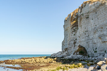 A rocky shoreline with a blue ocean in the background in Normandy France. The ocean is calm and the rocks are jagged