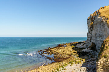 A rocky shoreline with a blue ocean in the background in Normandy France. The ocean is calm and the rocks are jagged