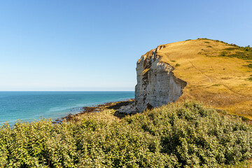 A rocky shoreline with a blue ocean in the background in Normandy France. The ocean is calm and the rocks are jagged
