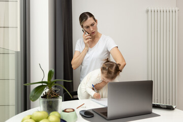 Young mom during a phone call with her clients. Multitasking mom working in her home office with her baby