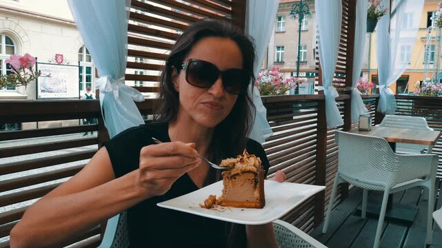Slow motion close-up video of a Caucasian woman enjoying a sweet dessert at a beautifully designed outdoor caf&eacute; on a sunny summer day