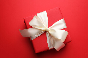 Beautiful gift with bow on red background, top view