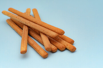 A group of golden crisp Italian bread cracker sticks forms a delicious and crunchy savory appetizer against a pastel blue backdrop. Perfect for menu design. Selective focus.
