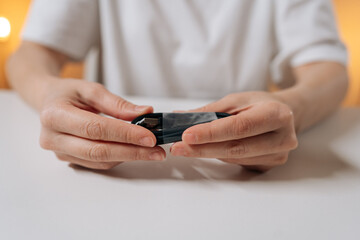 Person hands untangling knotted black power cord sitting at white table, preparing charging cable for use and restoring order to tangled wire.