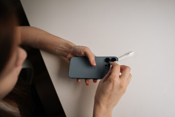 Top view of woman cleaning smartphone camera lens with cotton swab, maintaining crisp image clarity sitting at white table, showcasing careful device maintenance. Concept of modern technology.
