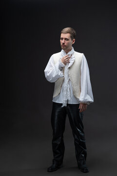 Young man in early Baroque suit with lace blouse and unbuttoned vest on gray.