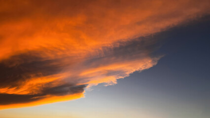 Sunset clouds with a dramatic formation, reddish and bright orange in color on the horizon, blending into a soft transition toward blue-gray at the bottom left.