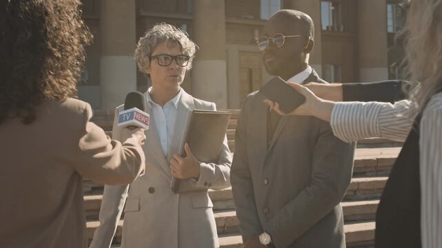 Medium full shot of annoyed Caucasian female barrister and security guard in business suits walking through crowd of reporters with microphones after court hearing, refusing to comment on case