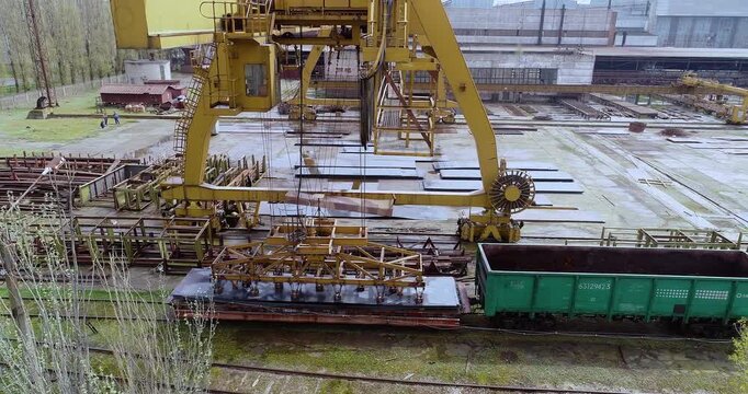 Gantry crane lifting steel sheets with electromagnet in metal warehouse. Overhead gantry crane loading steel sheets with magnet