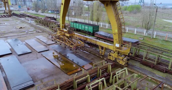 Gantry crane lifting steel sheets with electromagnet in metal warehouse. Overhead gantry crane loading steel sheets with magnet