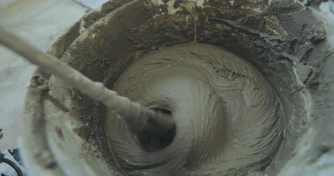 Mixing tile mortar for laying ceramic tiles or porcelain tiles. A man kneads tile mortar in a bucket with a paddle mixer or a paddle mixing drill. Close-up