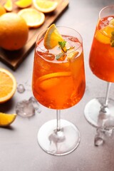Glasses of refreshing spritzer cocktail and oranges on grey table
