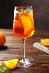 Glass of refreshing spritzer cocktail and oranges on wooden table