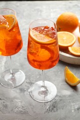 Glasses of refreshing spritzer cocktail and oranges on grey textured table