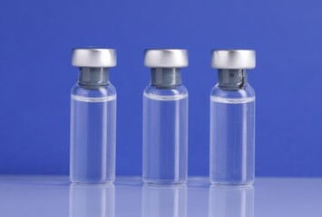 Vaccine in glass vials on light mirror surface against blue background, closeup