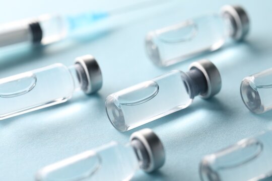 Vaccine in vials and syringe on light blue background, selective focus