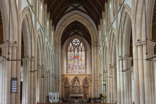 Interior of Holy Name Cathedral, Mumbai. Features Gothic architecture, soaring stone pillars, a detailed stained-glass window, and a wooden vaulted ceiling in a serene, sacred atmosphere.