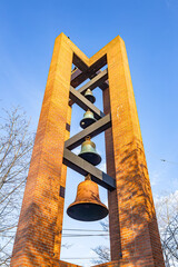 Brick bell tower with multiple bronze bells against clear blue sky.