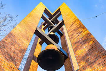 Brick bell tower with multiple bronze bells against clear blue sky.