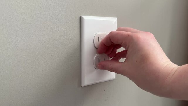 Female hand removing child safety outlet covers from an electrical wall socket. 