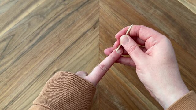 Female hands using a wooden cuticle pusher to gently push back cuticles during a nail care routine on a wooden table. 