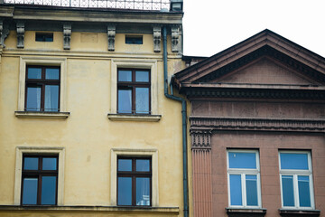 Close-up of two adjacent old buildings with classic architectural details, yellow and brown facades, and multiple windows. Suitable for illustrating urban architecture, city history, or real estate © Andriana Hoshko