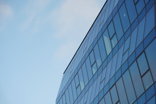 Contemporary office building with geometric glass facade reflecting the blue sky, photographed from a low angle. Suitable for illustrating architecture, business, or urban development concepts.