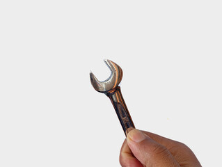 A closeup view of a hand holding a small open-end wrench against a clean white background, highlighting a simple, functional, and durable tool used for repair and mechanical tasks.